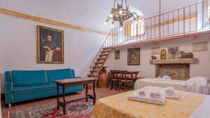 A room with a blue sofa, a yellow bed, a wooden table, and a staircase leading to an upper level. - Palazzo Danesi (Montepulciano)