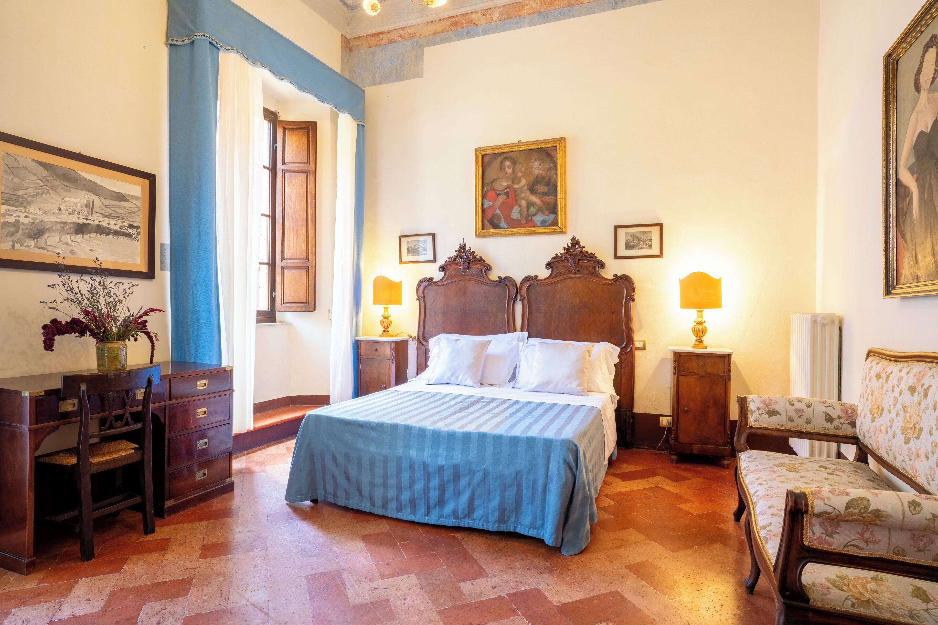 Un dormitorio con una cama grande, cabecera de madera, dos mesitas de noche con lámparas, cómoda de madera y una silla.