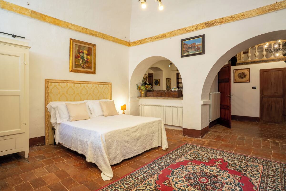 A bedroom with a bed, a nightstand, a dresser, and a large window.