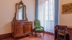 A room with a wooden cabinet, a green upholstered chair, and a mirror. - Palazzo Danesi (Montepulciano)