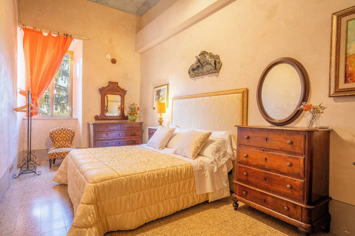 A bedroom with a bed, dresser, chair, and a window with curtains.