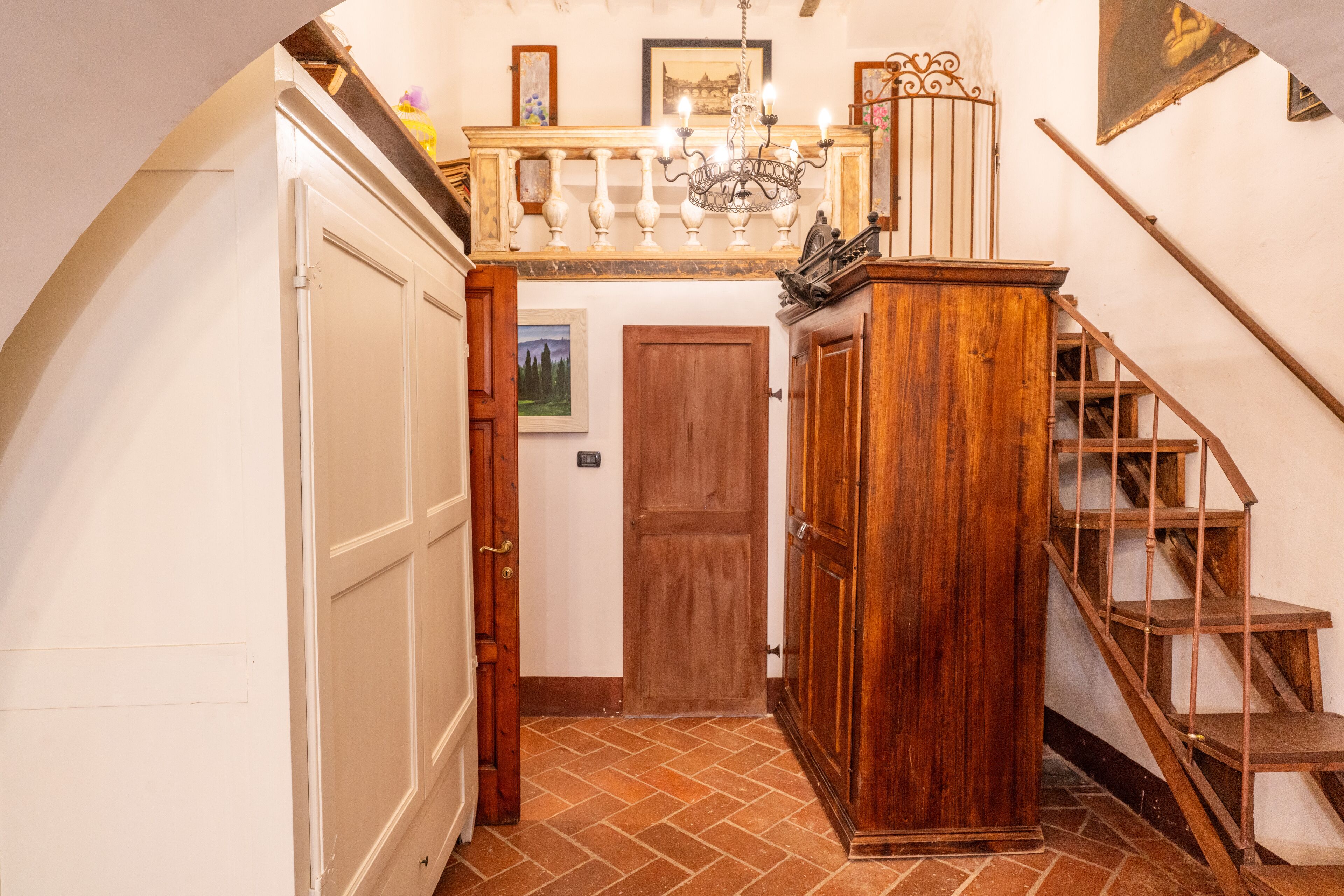 A hallway with a wooden staircase, a chandelier, and a door leading to another room.