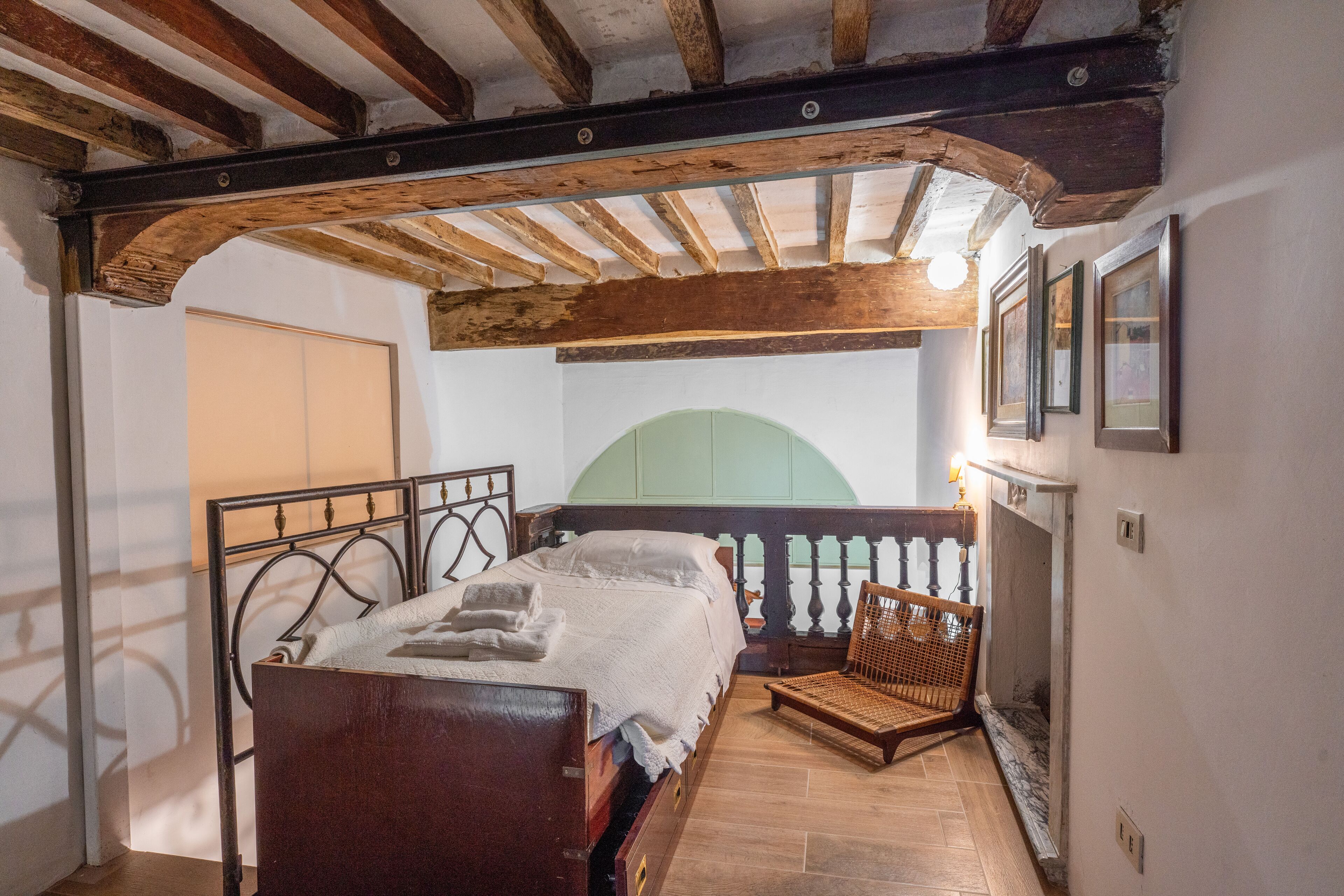 Een slaapkamer met een houten bed, een rieten stoel en uitzicht op de stad door een raam.