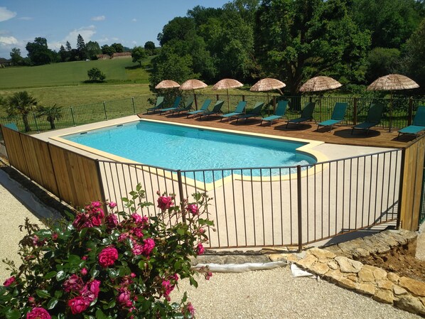A rectangular swimming pool with a wooden deck and a metal fence. There are several green lounge chairs and thatched umbrellas. - Magnificent estate for 18 guests with a private heated pool in Sarlat (Prats-de-Carlux)