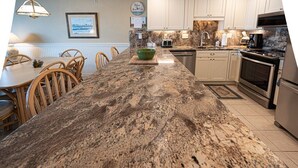 Una cocina con encimera de granito, sillas de madera, una mesa de comedor y un microondas.