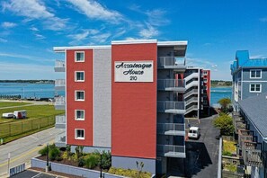 A multi-story building with balconies, labeled "Assateague House 210," located near a body of water.