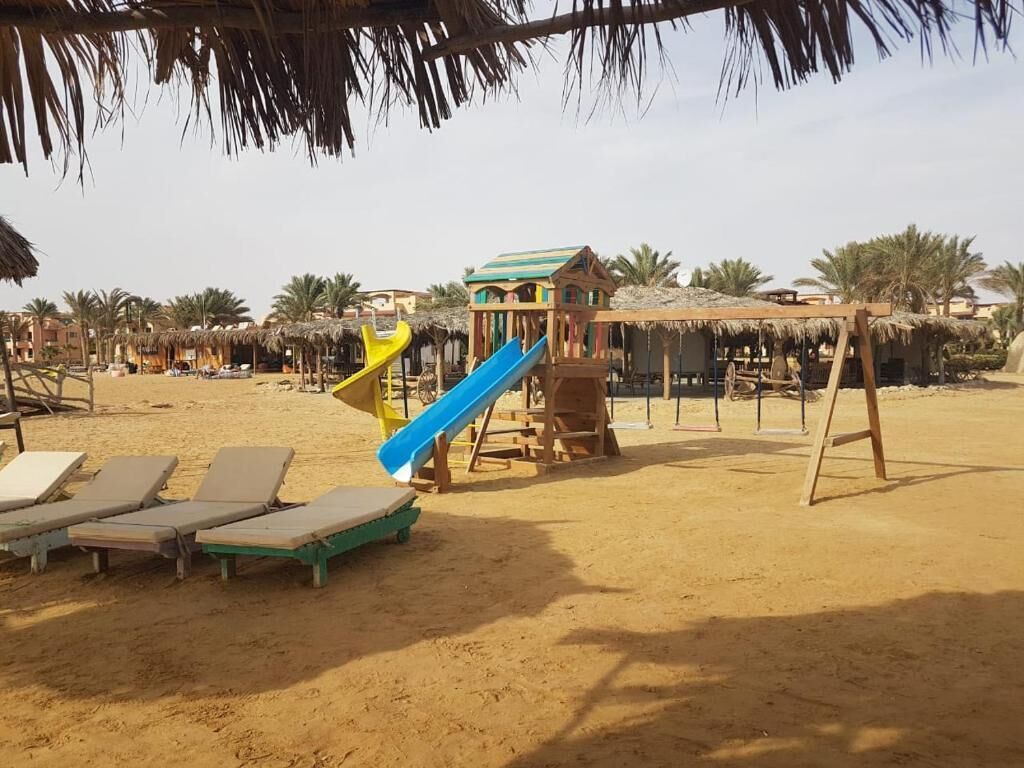 Una playa con un área de juegos que incluye un tobogán y una pequeña casita.