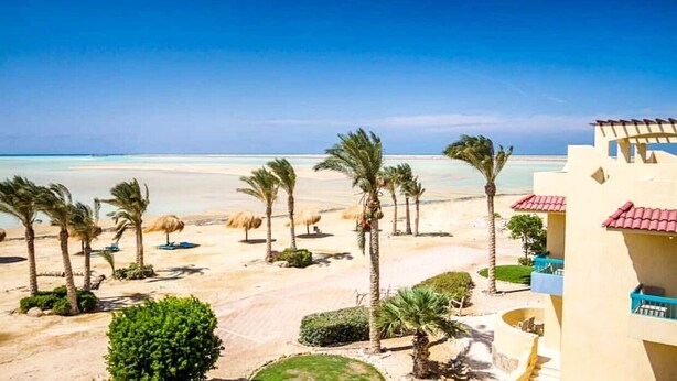 Ein Strandresort mit Palmen, einem Sandstrand und einem Gebäude mit Balkonen.