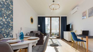 A modern living room with a dining area, a sofa, a TV, and a balcony with a view of the city.