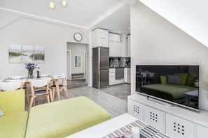A modern apartment with a dining area, kitchen, living room, and a large TV.
