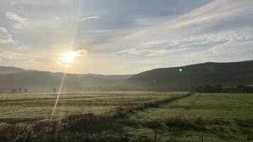 A rural landscape with a sunrise or sunset, fields, and distant hills.
