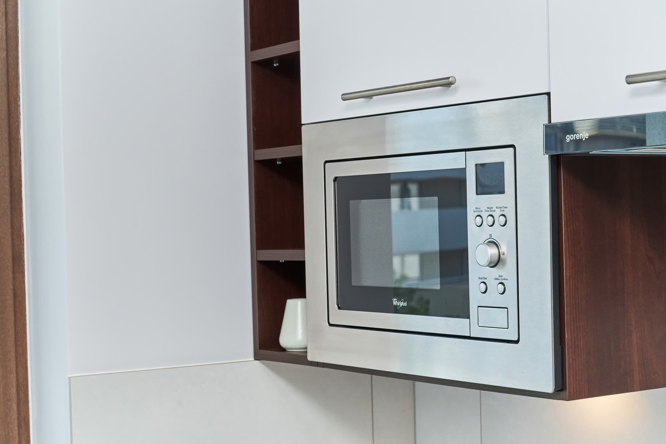 A modern kitchen with a built-in microwave, a handle above it, and a wooden cabinet below.