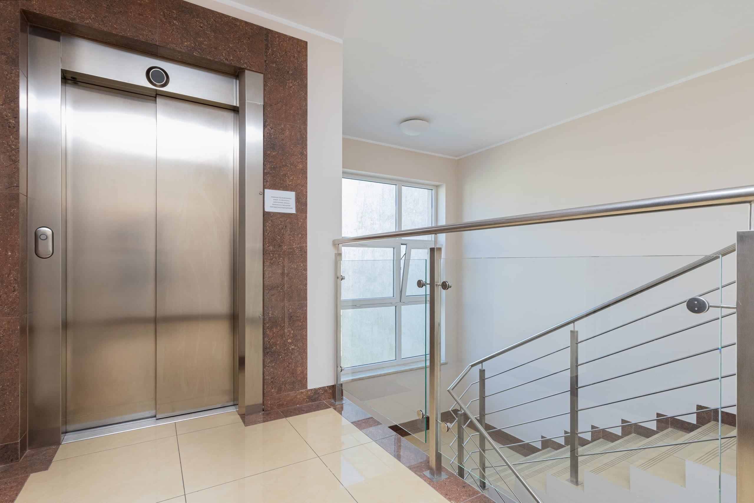 An elevator, a staircase with glass railings, and a window.