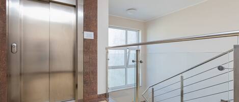 An elevator, a staircase with glass railings, and a window.