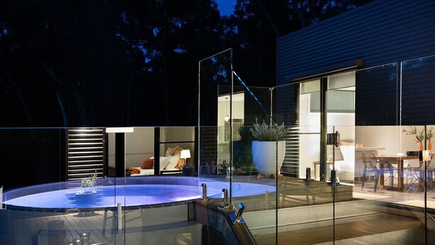 A modern outdoor pool area with glass walls, a hot tub, and a well-lit interior space. - Kangary- secluded bush retreat with spa (Daylesford)