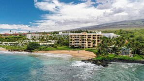 Un hotel frente a la playa con varias construcciones, una playa de arena y vistas al océano.