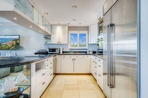 A modern kitchen with white cabinets, stainless steel appliances, and a large window with a view of the outdoors.