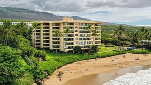 A multi-story hotel with a flat roof, surrounded by lush greenery and a beach. - Unbeatable Ocean Vistas at Polo Beach Club #606 – Beachfront Living in Wailea (Makena, Maui)