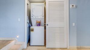 A laundry room with a washer and dryer, a door with louvered panels, and a small step leading to the room. - Unbeatable Ocean Vistas at Polo Beach Club #606 – Beachfront Living in Wailea (Makena, Maui)