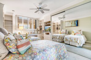 A bedroom with two beds, a desk, and a large window with shutters.