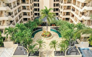 Un hotel de varios pisos con un patio central que cuenta con palmeras y una piscina.