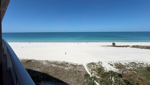 Vista de una playa con cielo despejado, arena y vegetación escasa.