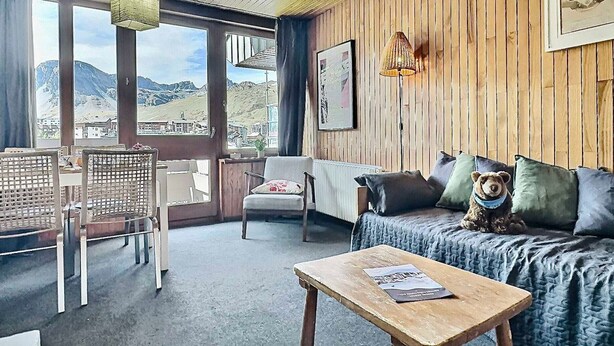 A cozy room with a wooden ceiling, a sofa with cushions, a table with a book, and a chair.