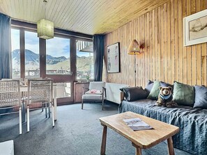 A cozy room with a wooden ceiling, a sofa with cushions, a table with a book, and a chair. - 2-room apartment, 4 people, near slopes, pets welcome (Tignes)