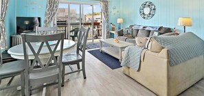 Un salon comprenant un canapé, un téléviseur, une table à manger avec des chaises, et une vue sur l’extérieur grâce à une porte vitrée.