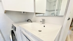 Casa de banho moderna com lavatório branco, espelho em cima e máquina de lavar à esquerda.