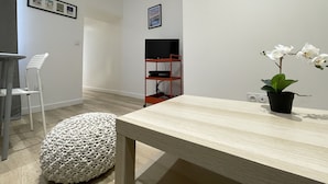 Uma sala de estar moderna com uma mesa de madeira, um banquinho branco, uma cadeira branca, uma TV sobre um suporte vermelho e um quadro na parede.