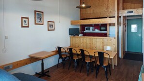 A dining area with a wooden table and chairs, a kitchen with appliances, and framed pictures on the wall.