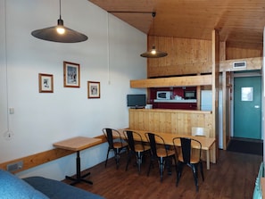 A dining area with a wooden table and chairs, a kitchen with appliances, and framed pictures on the wall.
