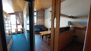 A room with a bunk bed, a sofa, a table, and a kitchenette.
