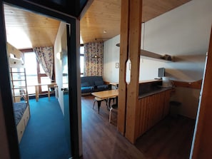A room with a bunk bed, a sofa, a dining table, and a kitchen area with a counter and appliances.