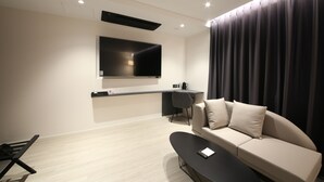 A modern living room with a flat-screen TV mounted on the wall, a sofa, a coffee table, and a desk with a chair. - Hotel Stay Gumi (Gumi)