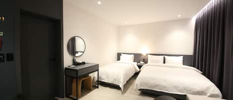 Quarto de hotel moderno com duas camas, uma escrivaninha com espelho, mesa de cabeceira e uma janela grande com cortinas.