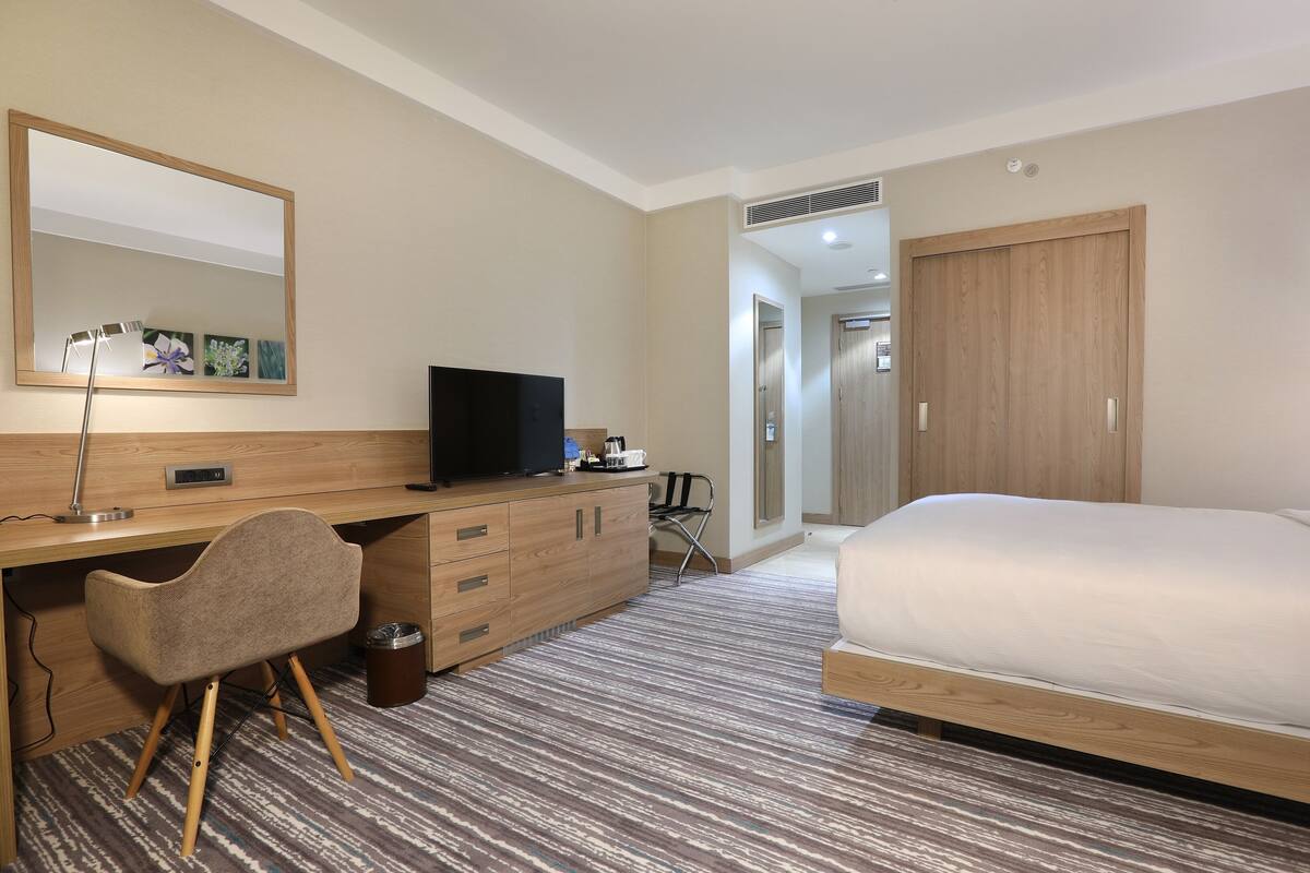 A hotel room with a bed, a desk with a chair, a television, and a wardrobe.