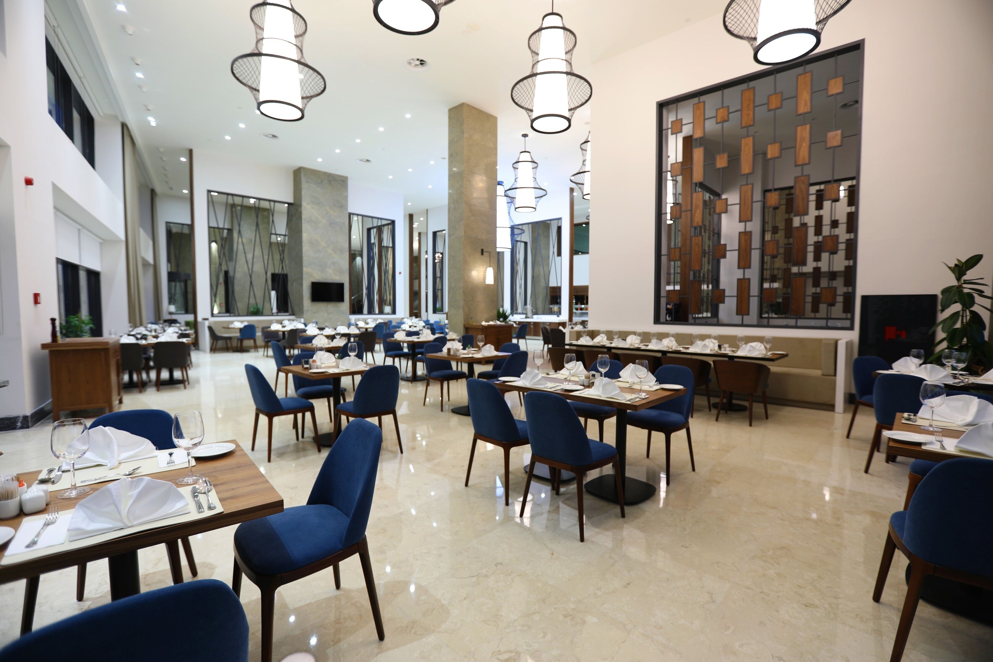 A spacious dining area with multiple tables and chairs, modern lighting fixtures, and a large decorative wall.