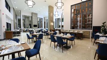 A spacious dining area with multiple tables and chairs, modern lighting fixtures, and a large decorative wall.