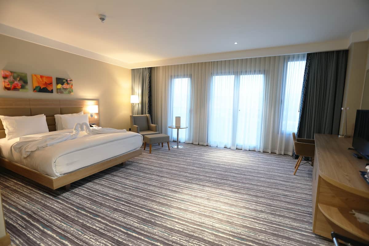A hotel room with a large bed, a desk, a chair, a small table, and a TV.