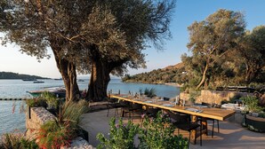 An outdoor dining area with a long wooden table set for four, surrounded by stone walls and potted plants. - Bobo by The Stay (Bodrum)