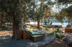 An outdoor seating area with wooden benches and a green cushioned bench, surrounded by trees and rocks near a body of water. - Bobo by The Stay (Bodrum)