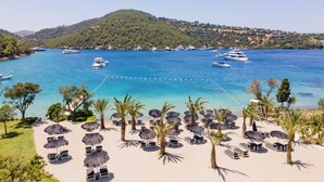 A beach with sun loungers and umbrellas, a clear blue sea, and yachts docked in the background. - Bobo by The Stay (Bodrum)
