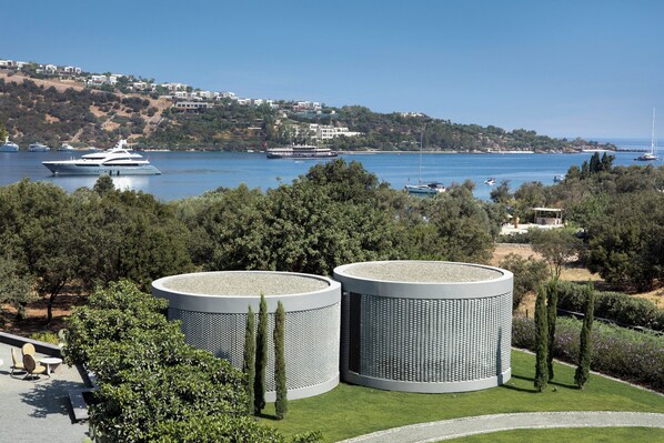 A coastal view with a modern building featuring cylindrical structures, a marina with boats, and a hillside with buildings. - Bobo by The Stay (Bodrum)