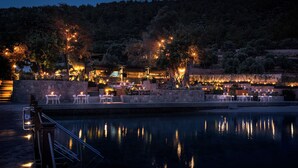 A waterfront restaurant with outdoor seating by a pool, surrounded by trees and a stone wall. - Bobo by The Stay (Bodrum)