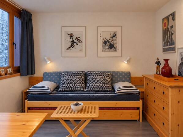 A cozy room with a sofa, a wooden table, and a dresser. There are two framed pictures on the wall.