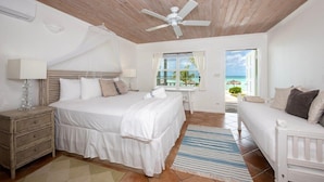Quarto com cama, mesas de cabeceira, ventilador de teto, janela com vista para a praia e varanda.