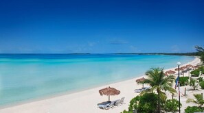 A beach with clear turquoise water, white sand, and a row of sun loungers and thatched umbrellas.