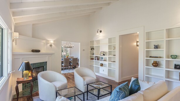 Uma sala de estar ampla com lareira, sofás brancos, uma mesa de centro de vidro e uma estante.
